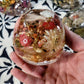Top view of pink resin skull surrounded by preserved pinecones and flowers
